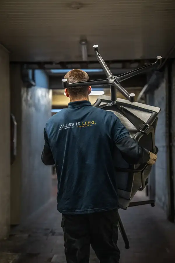 Medewerker van Alles Is Leeg draagt een bureaustoel naar buiten